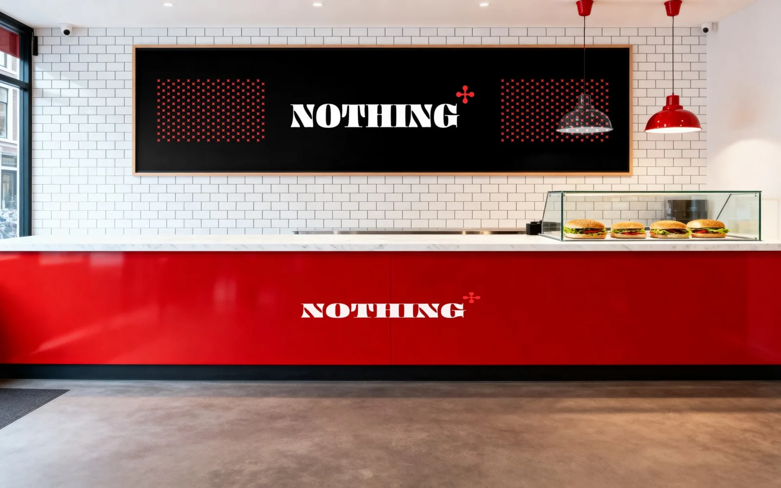 Dentro: un bancone rosso con il logo bianco «NOTHING», piastrelle bianche dietro e una lavagna nera con il logo tra due campi del motivo.