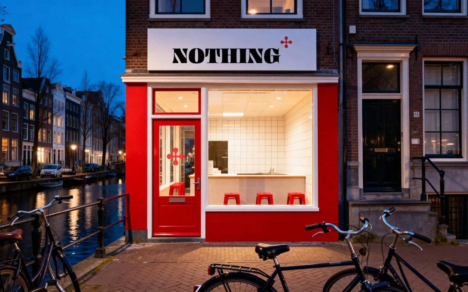Una facciata rossa lungo un canale di Amsterdam al crepuscolo, il logo «NOTHING» su un’insegna bianca sopra la vetrina e il segno sul vetro della porta, biciclette davanti.